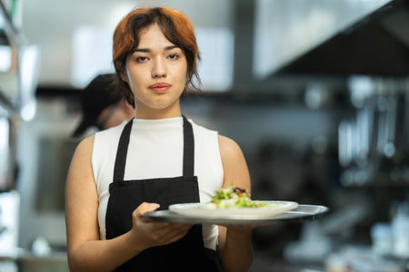 Young female with prepared dish in restaurant kitchenの写真素材