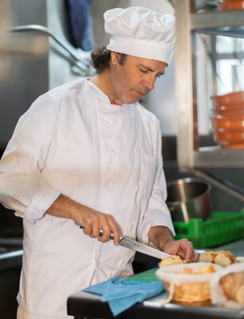 Adult male chef slicing bread in kitchen