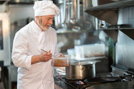 Eldery male chef prepares dish in frying pan
