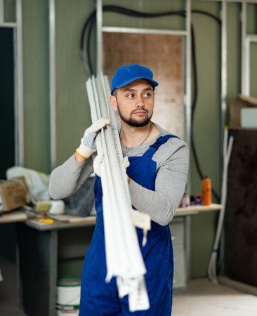 Builder in blue overalls arranging metal square tubes while preparing materials for work in building under renovationの写真素材