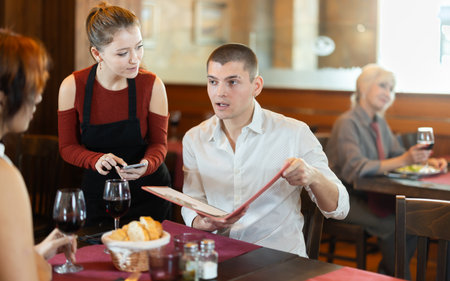 Young waitress taking order from young couple in restaurantの写真素材