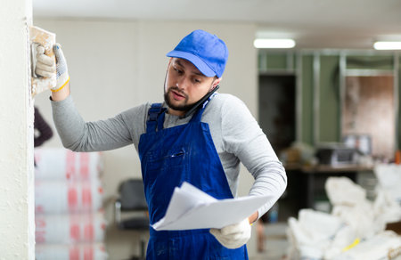 Master in blue overalls talking on mobile phone, discussing documents in renovated buildingの写真素材