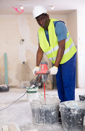 Male builder mixing plaster in bucket using electric mixer closeupの写真素材