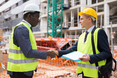 Successful architect and engineer shake hands on construction site