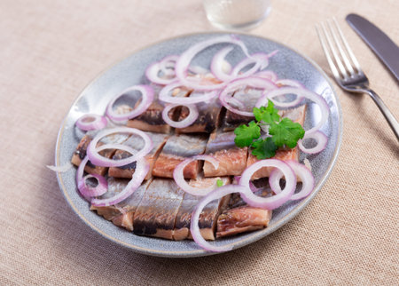 on wooden table stands plate with pieces herring fillet, garnished with onion rings and parsleyの写真素材