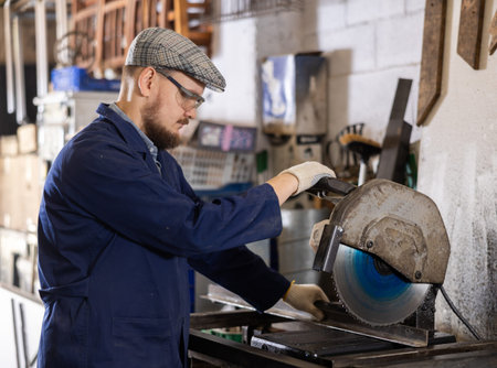 Work in metalworking shop - man wearing safety glasses cuts a metal corner with circular saw