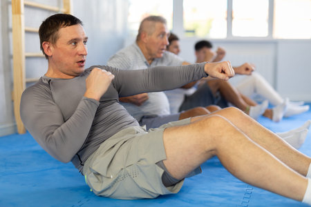 Group of men performing combat strikes sitting during group training
