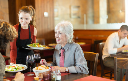 Young waitress bringing food to adult couple in restaurantの写真素材
