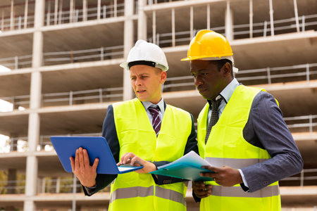 Architect and foreman must write documents and drawings on laptop with building construction