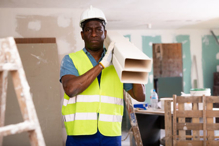 African-american man builder carries square plastic pipes on shoulder
