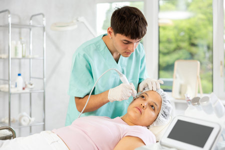 Young male cosmetologist doing microcurrent procedure to young woman