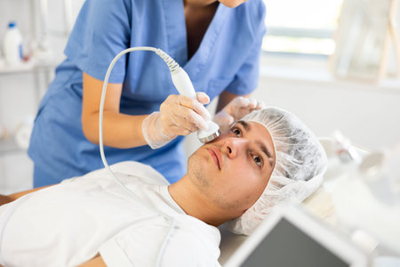 Young woman cosmetologist doing ultrasound procedure to young man