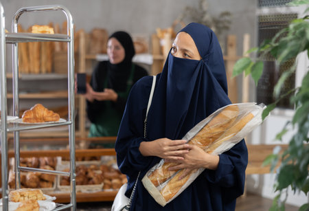 Middle-aged Muslim woman chooses pastry with muslim seller in background in bakeryの写真素材