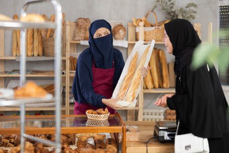 Muslim saleswoman gives baguettes to Muslim girl in bakeryの写真素材