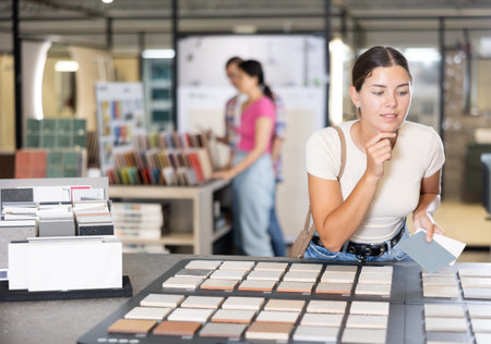 Girl exploring tile samples on display board in building hypermarket