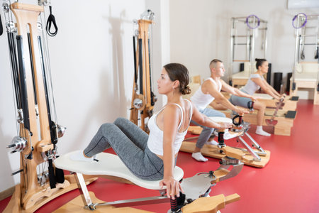 Young woman stretches her arms using pilates reformer while sitting backwards