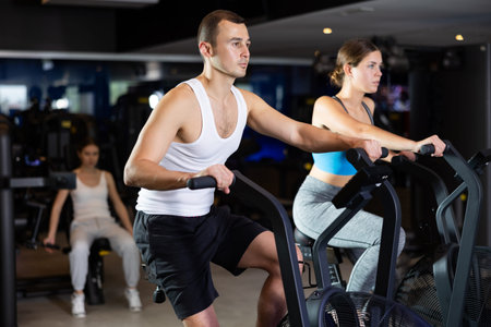 Sportive young couple doing air bike exercises in well-equipped gym