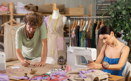 Middle-aged male dressmaker drawing with curves while woman sewing