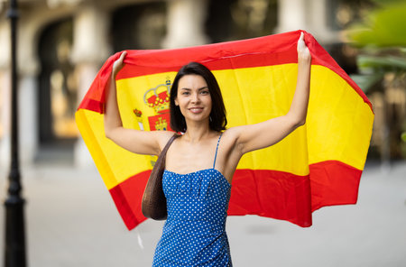 Patriotic young brunette girl waving the flag of Spain on city streetの写真素材