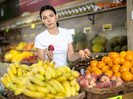 Woman near vegetable stand in store choose flat peachの写真素材