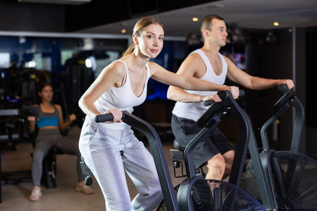 Sportive young couple doing air bike exercises in well-equipped gym