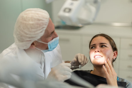 Mature man doctor dentist in white coat examines oral cavity of girl patient in dentistry.の写真素材