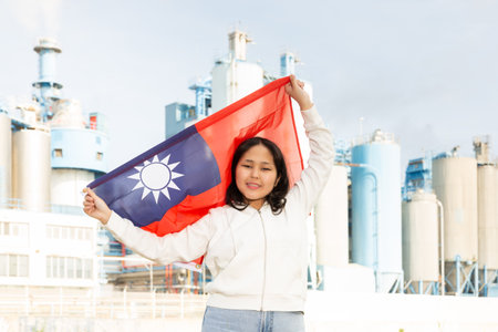Happy young woman with flag of Taiwan against background of factoryの写真素材