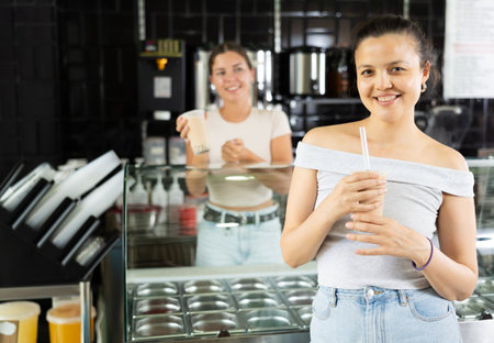 Satisfied joyful asian girl drinking tea with bubble milk in cafeの写真素材
