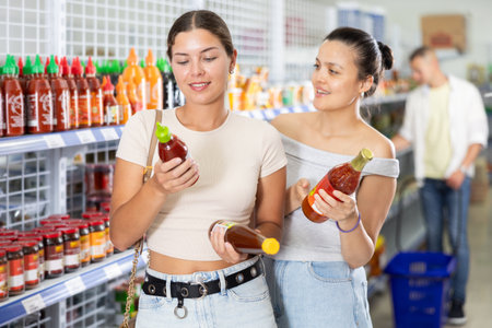 Two female friends choose spicy sauce sauce in Chinese supermarket. Read the QR code from the label using smartphoneの写真素材
