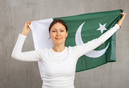 Positive middle-aged woman holding state flag of Pakistan against gray wall background indoorsの写真素材
