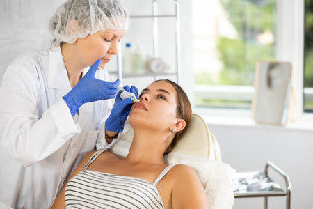Doctor gives injection and performs procedure of lip augmentation of girl patient in clinic.の写真素材