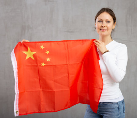 Happy young woman holding flag of China against unicoloured backgroundの写真素材