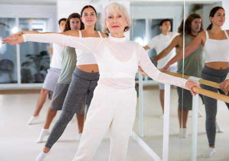 Elderly female dancer exercise near the ballet barre at a group training session in the dance studio.の写真素材