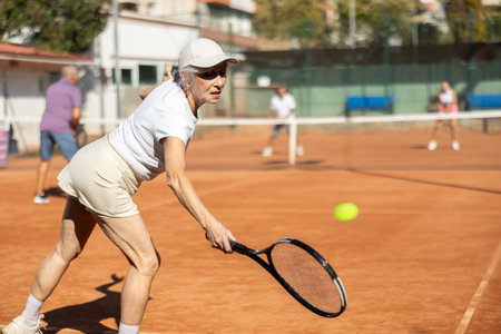 Positive active old woman preparing to strike and return ball to opponents field during doubles match in tennis clubの写真素材