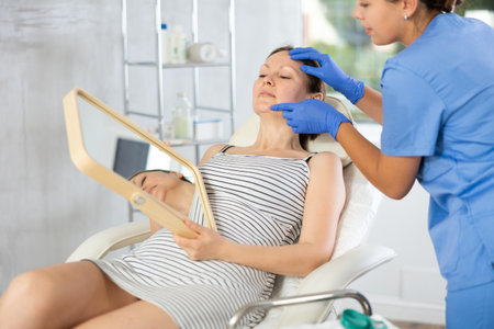 Woman cosmetologist examines patients face after lifting procedure and palpates chin areaの写真素材