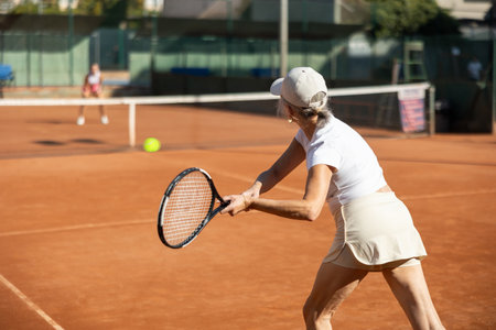 Rear view of focused european aged woman playing tennis match in court of tennis clubの写真素材