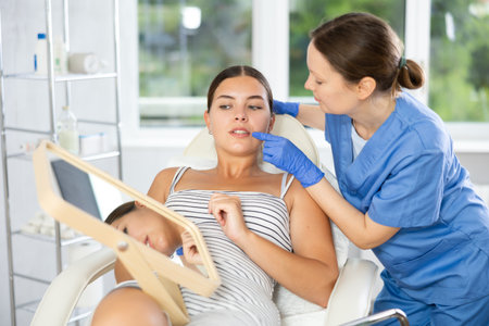 Adult female cosmetologist examining face of female patientの写真素材