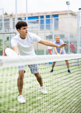 Sportive young man playing padel together with a partner. View through tennis netの写真素材