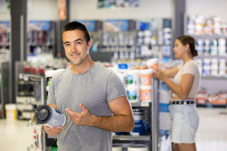 Smiling man standing in hardware store with can of paintの写真素材