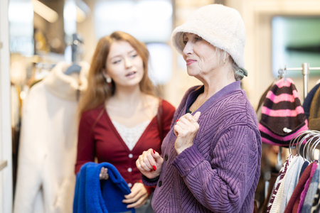 Positive girl and mature woman trying hat in clothing storeの写真素材