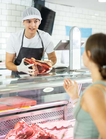 Young male seller offers girl to buy fresh beef entrecote boneless meatの写真素材
