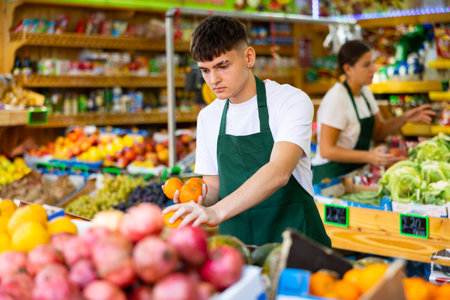 Hardworking young salesman puts fresh oranges on the counterの写真素材
