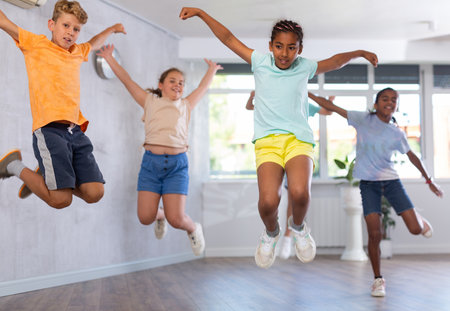 Group of positive juvenile boys and girls jumping cheerfully in dancehallの写真素材