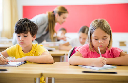 Focused preteen pupils studying in classroom with female teacher
