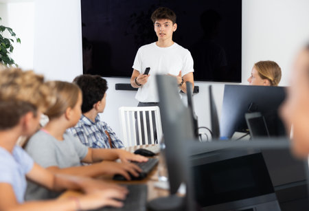 Friendly young teacher standing near an interactive whiteboard telling new material to teenage students in school computer classの写真素材