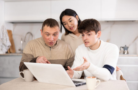 Adult man and young couple using laptop in kitchen