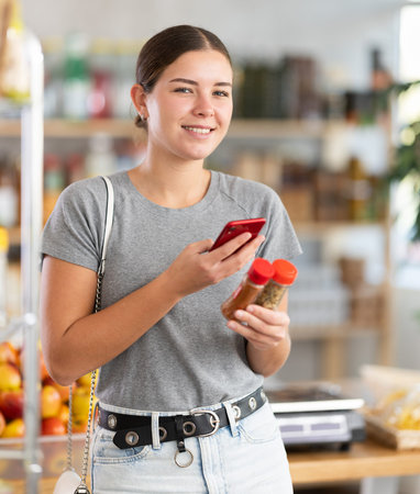 In shop youth girl scan QR code and take reading spices package bottle using phone camera