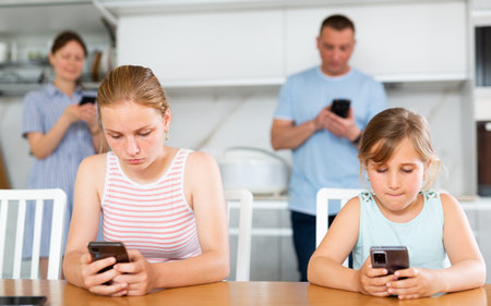 Sister girls sitting near kitchen table with phones in hands and flipping through tape