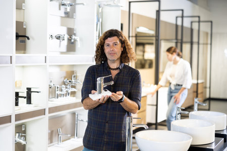 Man inspects and chooses new kitchen or bath tap faucet at hardware storeの写真素材