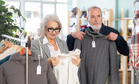 Elderly married couple chooses fashionable sweater in clothing storeの写真素材